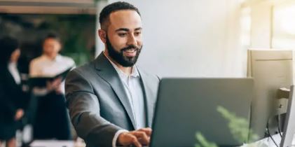 Smiling business professional working on a desktop computer in a modern office. Engaged in productivity and digital collaboration, reflecting efficiency and workplace success.
